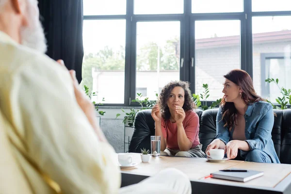 African american lesbian woman talking to blurred psychologist while sitting on sofa with girlfriend — Stock Photo