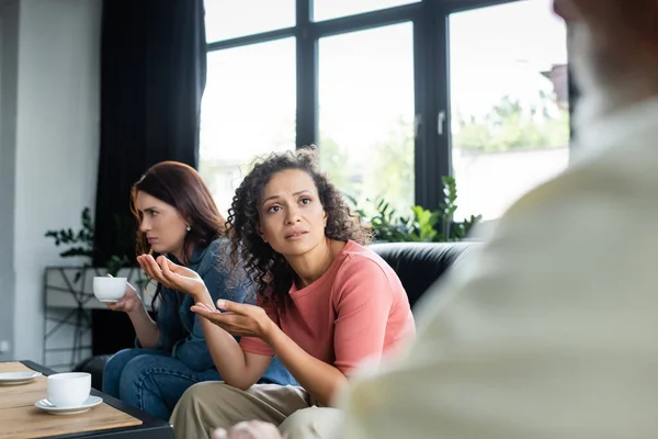 Mujer lesbiana afroamericana preocupada señalando a novia deprimida durante consulta con psicólogo borroso - foto de stock