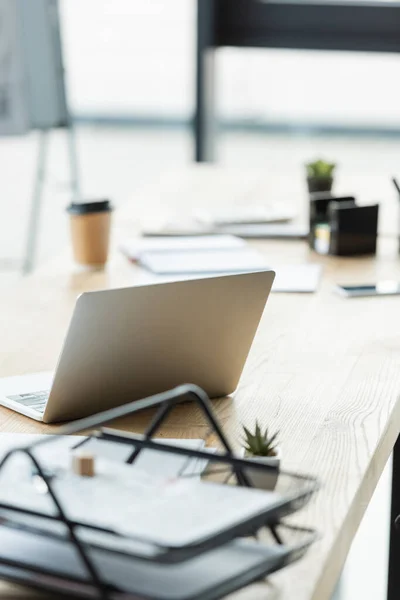 Selective focus of laptop near blurred papers and takeaway drink on office desk — Stock Photo