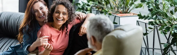 Alegre afroamericana mujer hablando con psicólogo cerca lesbiana novia en consultoría habitación, banner - foto de stock