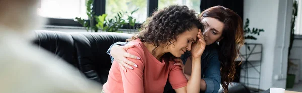 Mujer lesbiana abrazando llorando novia afroamericana durante cita con psicólogo, pancarta - foto de stock