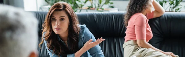 Lesbian woman pointing at depressed african american girlfriend during consultation with blurred psychologist, banner — Stock Photo