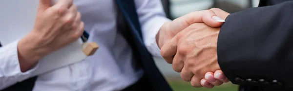 Partial view of businessman shaking hands with blurred realtor with digital tablet and key outdoors, banner — Stock Photo