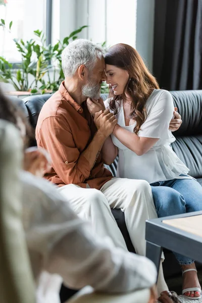 Complacida pareja abrazándose en sofá cerca borrosa afroamericana psicóloga en sala de consulta - foto de stock