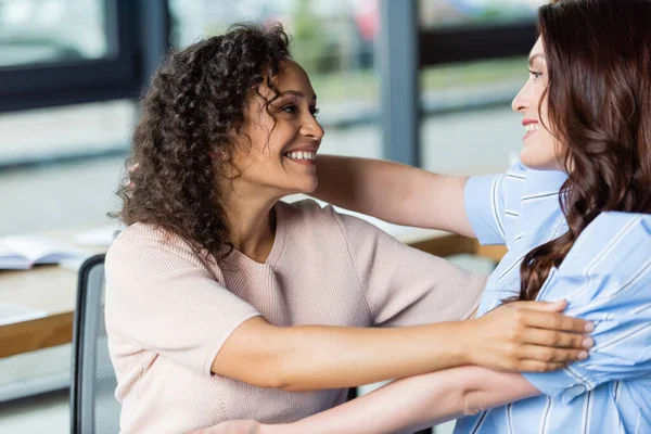 Joyful multiethnic lesbian couple embracing in real estate agency — Stock Photo