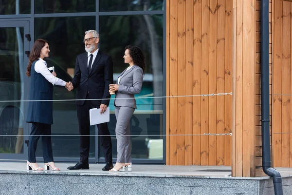 Empresario de mediana edad estrechando la mano con agente de bienes raíces cerca de socio de negocios afroamericano - foto de stock