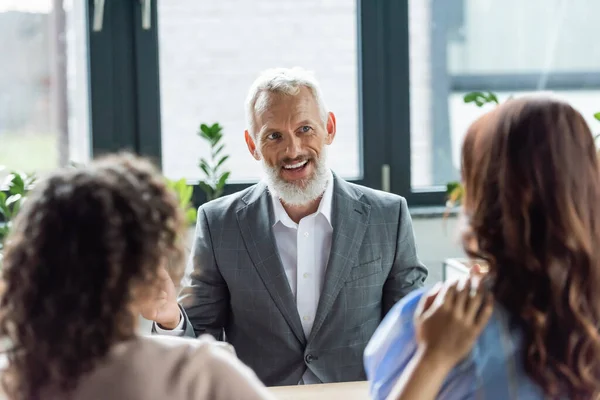 Back view of blurred interracial same sex couple near smiling broker in real estate agency — Stock Photo