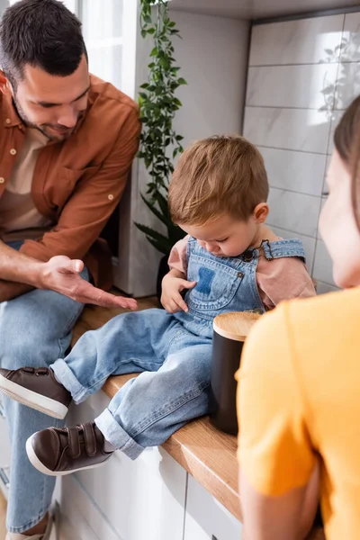 Petit garçon assis sur le plan de travail de la cuisine près des parents à la maison — Photo de stock