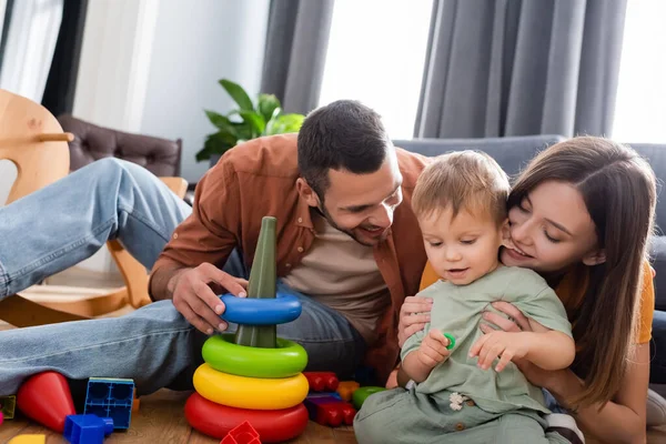 Fröhliche Eltern sitzen neben Sohn und Spielzeug im Wohnzimmer — Stockfoto