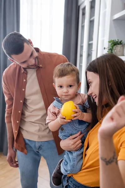 Toddler boy holding lemon near smiling parents at home — Stock Photo