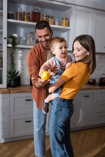 Sonriente padre sosteniendo limón cerca de esposa e hijo en la cocina - foto de stock