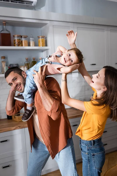 Padres positivos jugando con un niño pequeño en la cocina - foto de stock