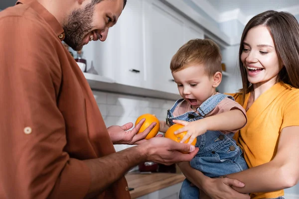 Mann hält Apfelsinen neben Kind und Frau zu Hause — Stockfoto