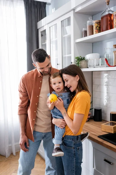 Щасливі батьки дивляться на маленького сина зі свіжим лимоном на кухні — стокове фото