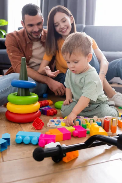 Enfant jouant avec des jouets près des parents flous dans le salon — Photo de stock