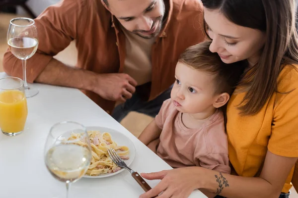 Padres mirando a su hijo cerca de la pasta y bebidas en casa - foto de stock