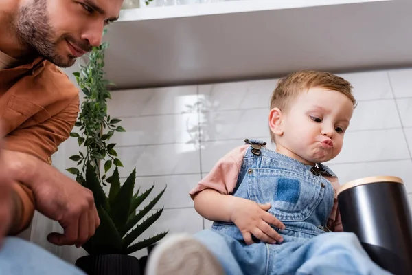 Low angle view of father looking at toddler child pouting lips in kitchen — Stock Photo