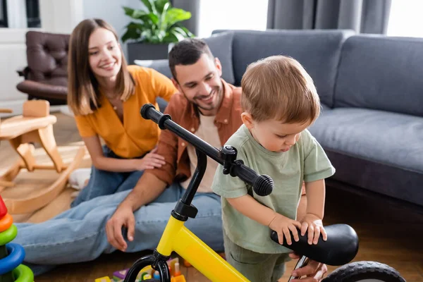 Маленький ребенок стоит рядом с велосипедом и родители дома — стоковое фото