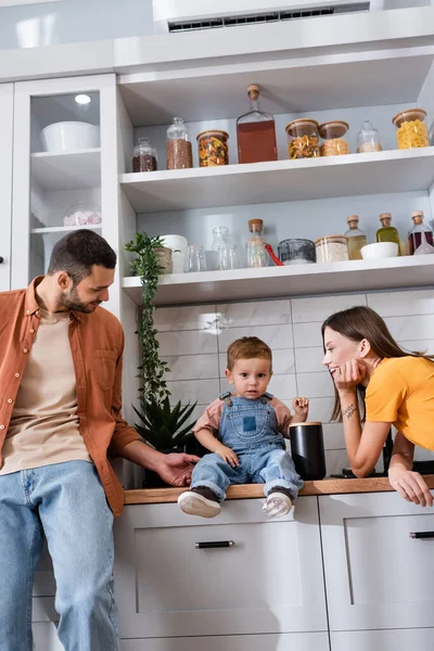 Jeunes parents regardant fils sur le plan de travail de la cuisine — Photo de stock