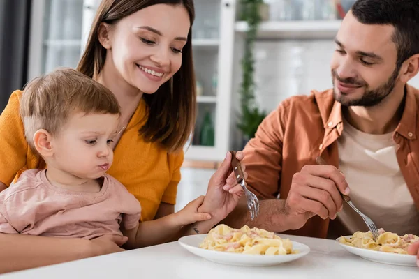 Улыбающаяся женщина держит вилку возле макарон и семьи дома — Stock Photo