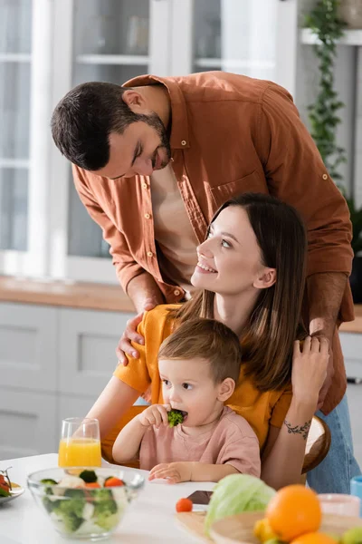 Hombre abrazando esposa cerca de hijo y verduras en cocina - foto de stock