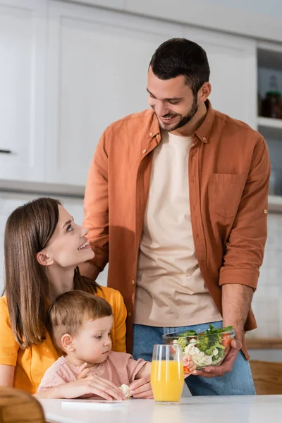 Hombre feliz sosteniendo ensalada cerca de esposa e hijo en casa - foto de stock