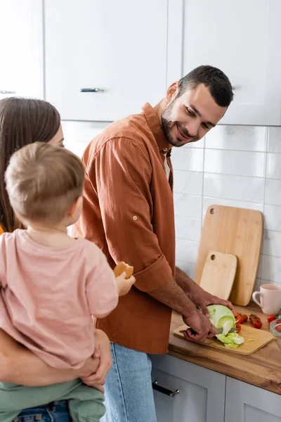 Hombre cortar col cerca borrosa familia en la cocina - foto de stock