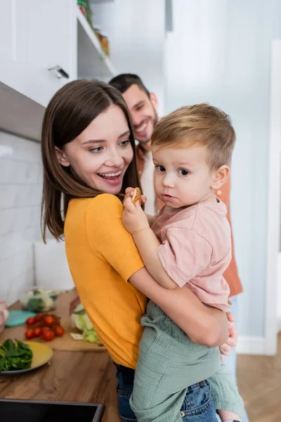 Mujer mirando hijo con galleta en cocina - foto de stock