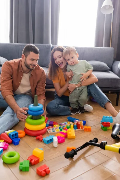 Smiling man holding toy near family and bike at home — Stock Photo