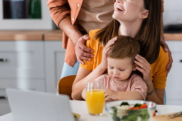 Frau umarmt Sohn neben Ehemann, Salat und Laptop zu Hause — Stockfoto