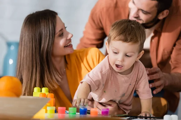 Enfant en bas âge jouant avec la peinture près des parents à la maison — Photo de stock