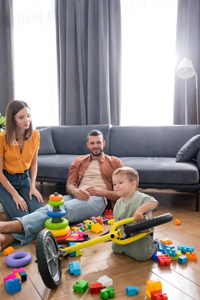 Les parents passent du temps avec un tout-petit fils tenant un vélo dans le salon — Photo de stock