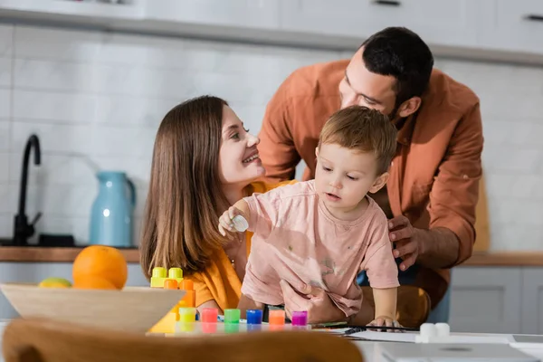 Feliz família abraçando filho perto de blocos de construção e dispositivos em casa — Fotografia de Stock