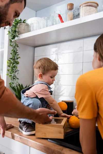 Tout-petit garçon tenant des oranges près des parents dans la cuisine — Photo de stock