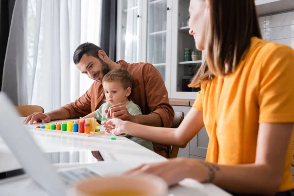 Father and child playing with educational game near mother using laptop — Stock Photo