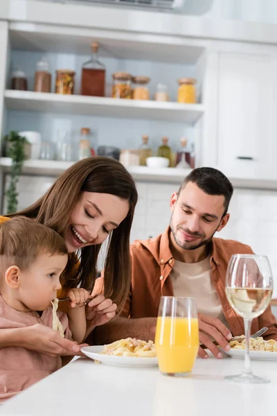 Woman feeding son with pasta near drinks and husband at home — Stock Photo