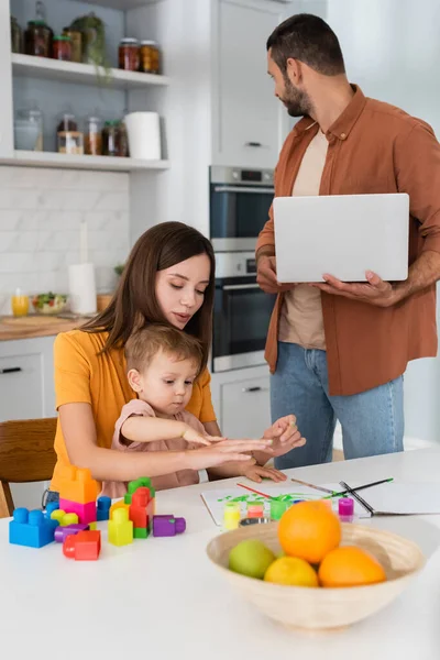 Mulher que trabalha com filho perto de blocos de construção e marido com laptop em casa — Fotografia de Stock