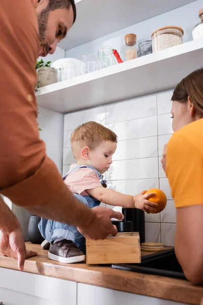 Pais em pé perto da criança com laranja na bancada da cozinha — Fotografia de Stock