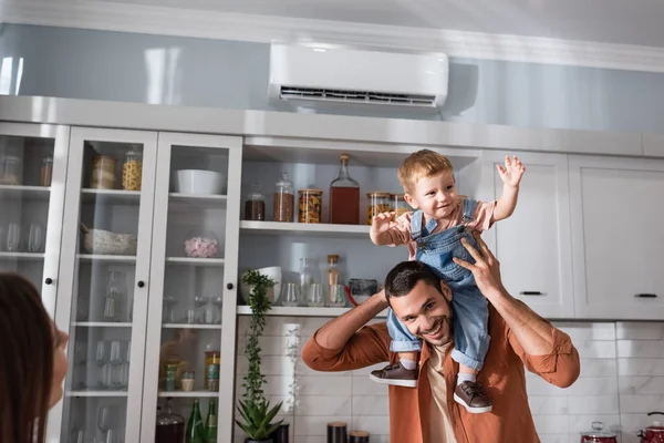 Pai feliz segurando filho criança perto da esposa borrada na cozinha — Fotografia de Stock