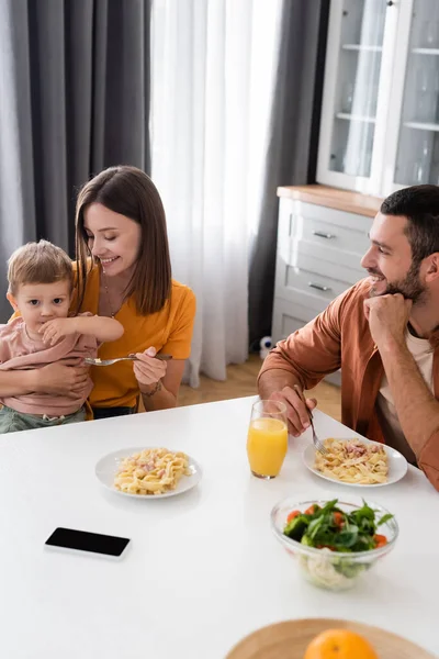 Позитивна сім'я, що сидить біля макаронних виробів, салату та смартфона вдома — стокове фото