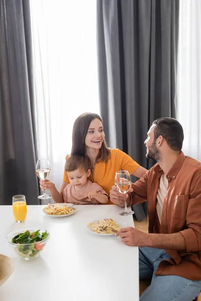Cheerful woman holding wine near husband and son during dinner at home — Stock Photo