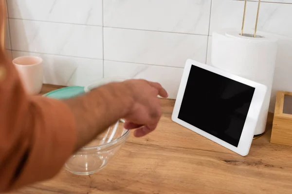Обрезанный вид человека указывая на цифровой планшет с пустым экраном возле миски на кухне — стоковое фото
