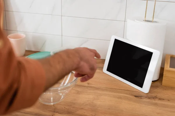 Vista recortada del hombre apuntando a la tableta digital con pantalla en blanco cerca del tazón en la cocina — Stock Photo