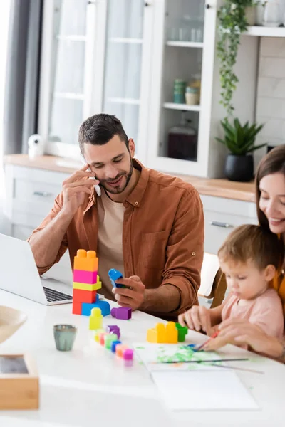 Freelancer sorridente falando em smartphones perto da família e blocos de construção — Fotografia de Stock