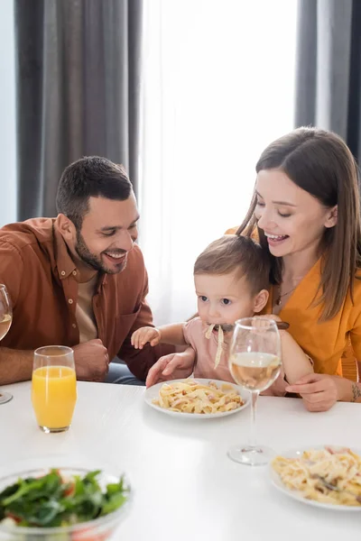 Positive parents looking at son eating pasta at home — Stock Photo