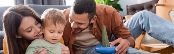 Happy parents looking at toddler son near toy at home, banner — Stock Photo