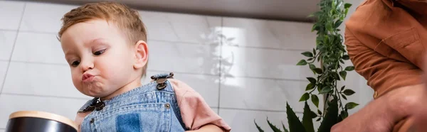 Low angle view of toddler kid pouting lips near dad in kitchen, banner — Stock Photo