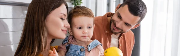 Lächelnde Eltern mit Zitrone in der Nähe ihres Kindes zu Hause, Transparent — Stockfoto