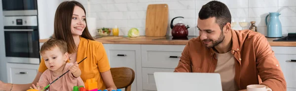 Mãe e filho com pincel sentado perto do marido com laptop, banner — Fotografia de Stock