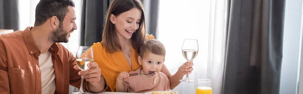 Smiling parents holding wine while son eating pasta at home, banner — Stock Photo